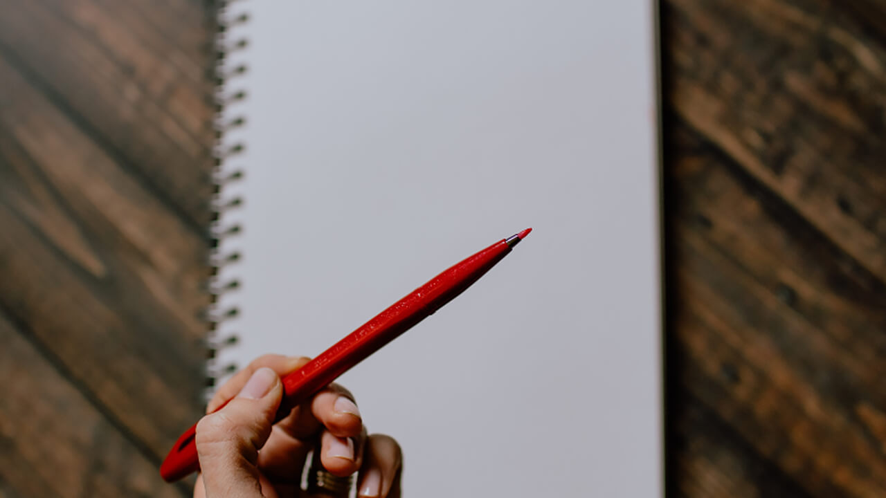 Person holding red pencil over notebook