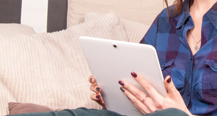 woman sitting on a couch and reading from a tablet